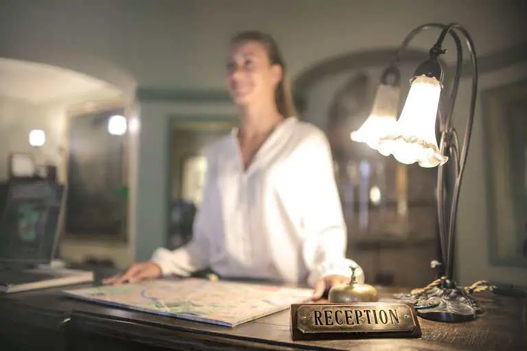 A concierge stands at a hotel reception desk under ambient lighting