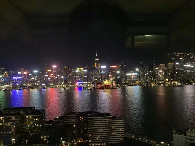 Victoria Harbour and the illuminated Hong Kong Island skyline at night, viewed from a Kimpton Tsim Sha Tsui guest room