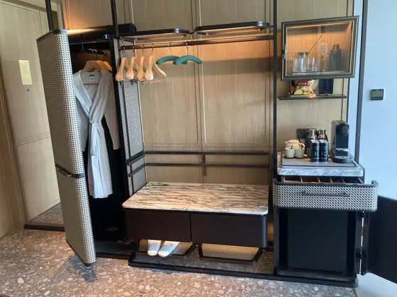 Well-stocked minibar beside an open wardrobe with two bathrobes in a guest room at Kimpton Tsim Sha Tsui Hong Kong.